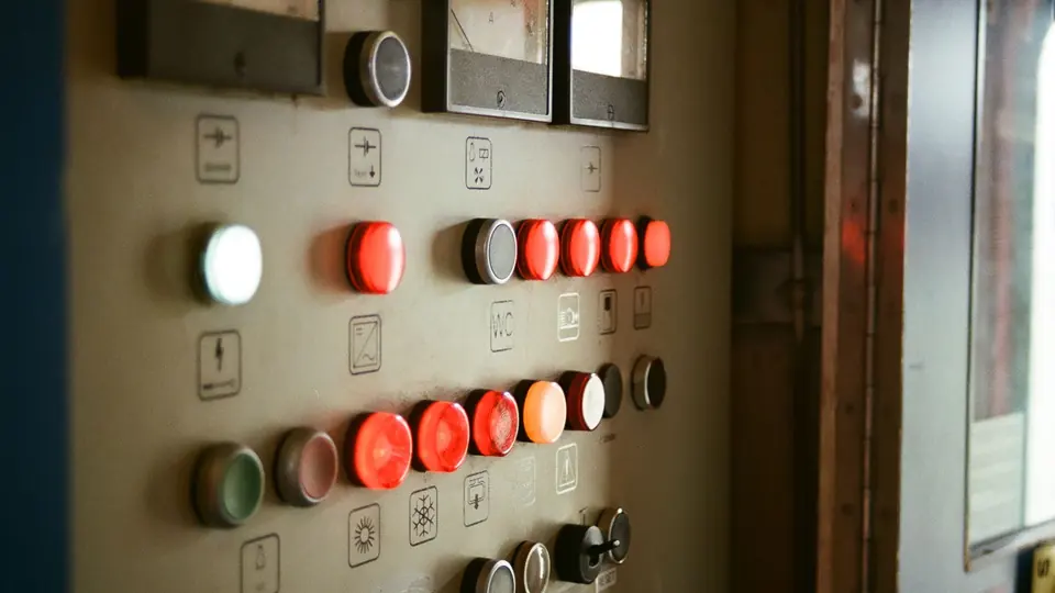 Industrial control panel with rows of illuminated push buttons, function symbols and analogue meters.